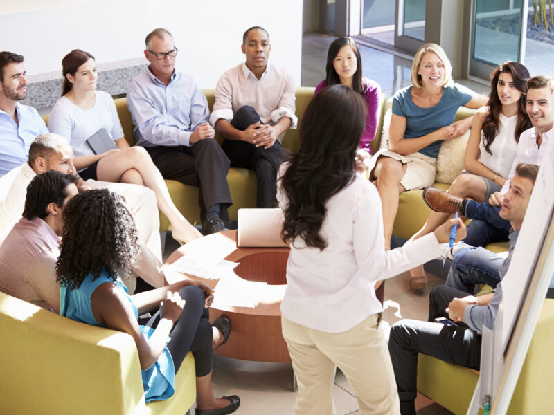 Businesswoman Making Presentation To Office Colleagues Meeting between staff members.
